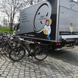 Bedrijfsbus van KDC Ontruimingen met cartoon-logo, geparkeerd naast fietsen op straat