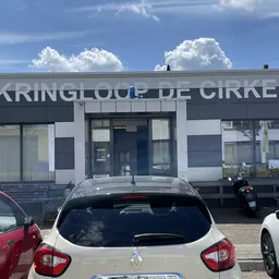 Gevel van Kringloop De Cirkel met winkelnaam op donkerblauw pand, geparkeerde auto's ervoor