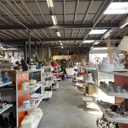 Binnenaanzicht van kringloopwinkel met stellingen vol huishoudelijke spullen, decoratie en diversen aan beide zijden van het 