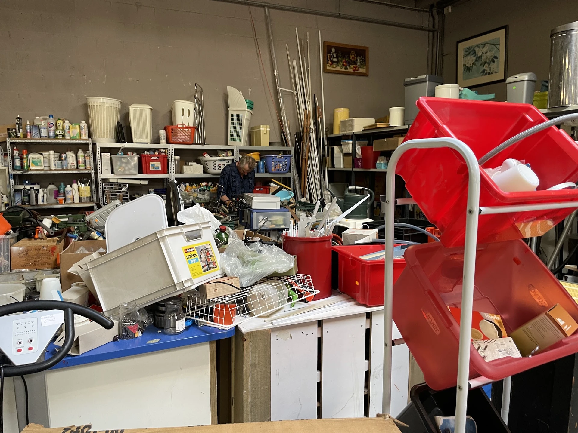 Binnenzicht van kringloopwinkel met stellingen, rode opbergboxen en diverse spullen
