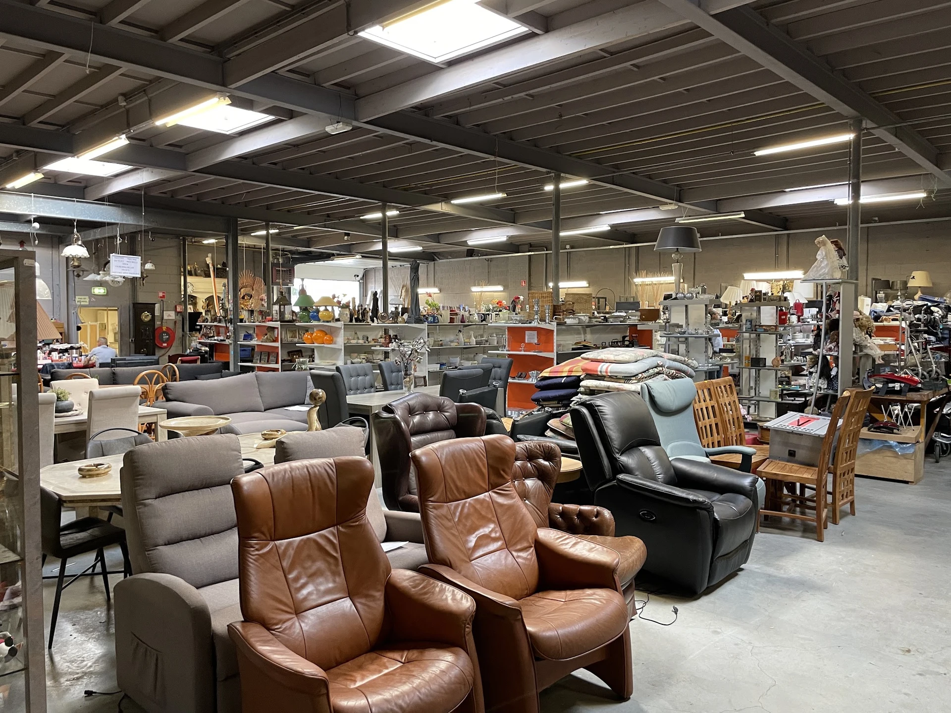 Winkelvloer met diverse meubels waaronder bruine lederen stoelen, grijze fauteuils en houten stoelen, onder fluorescente verl