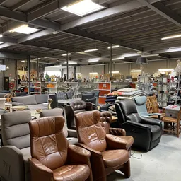 Winkelvloer met diverse meubels waaronder bruine lederen stoelen, grijze fauteuils en houten stoelen, onder fluorescente verl