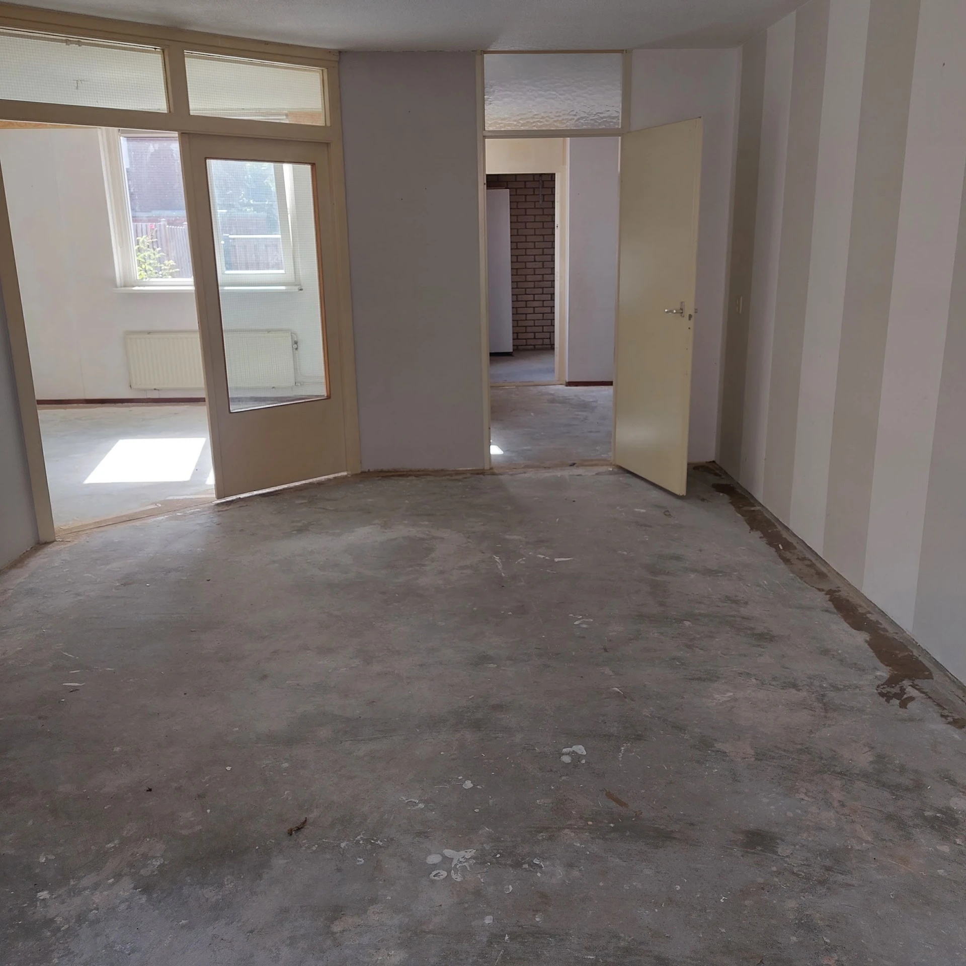 Lege winkelruimte met betonnen vloer, witte muren en open deuren naar andere kamers