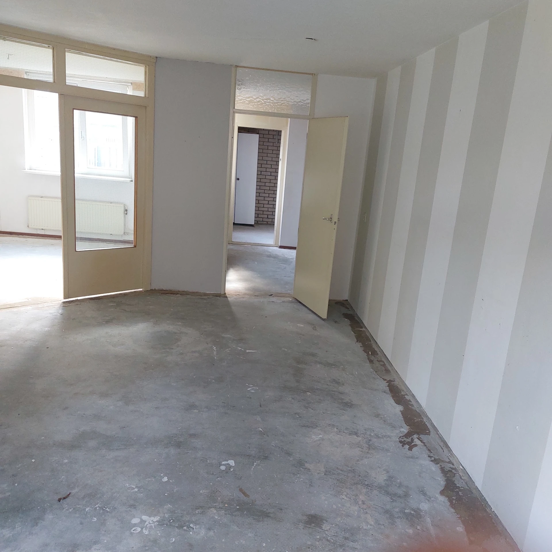 Lege winkelruimte met betonnen vloer, witte wanden en open deuren naar andere kamers