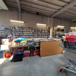 Overzicht van winkelruimte met stellingen vol media, dozen, huishoudartikelen en winkelwagens