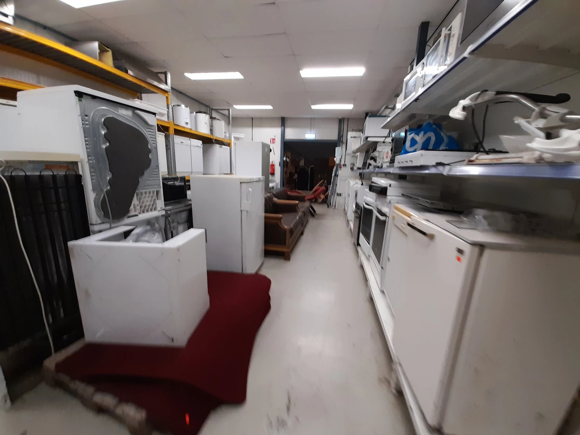Winkelinterieur met witgoedapparatuur en huishoudelijke artikelen uitgestald langs beide zijden van het gangpad