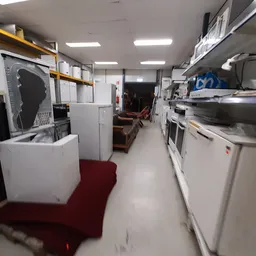 Winkelinterieur met witgoedapparatuur en huishoudelijke artikelen uitgestald langs beide zijden van het gangpad