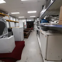 Binnenzicht van kringloopwinkel met witte huishoudapparatuur op stellingen en tafels langs beide zijden