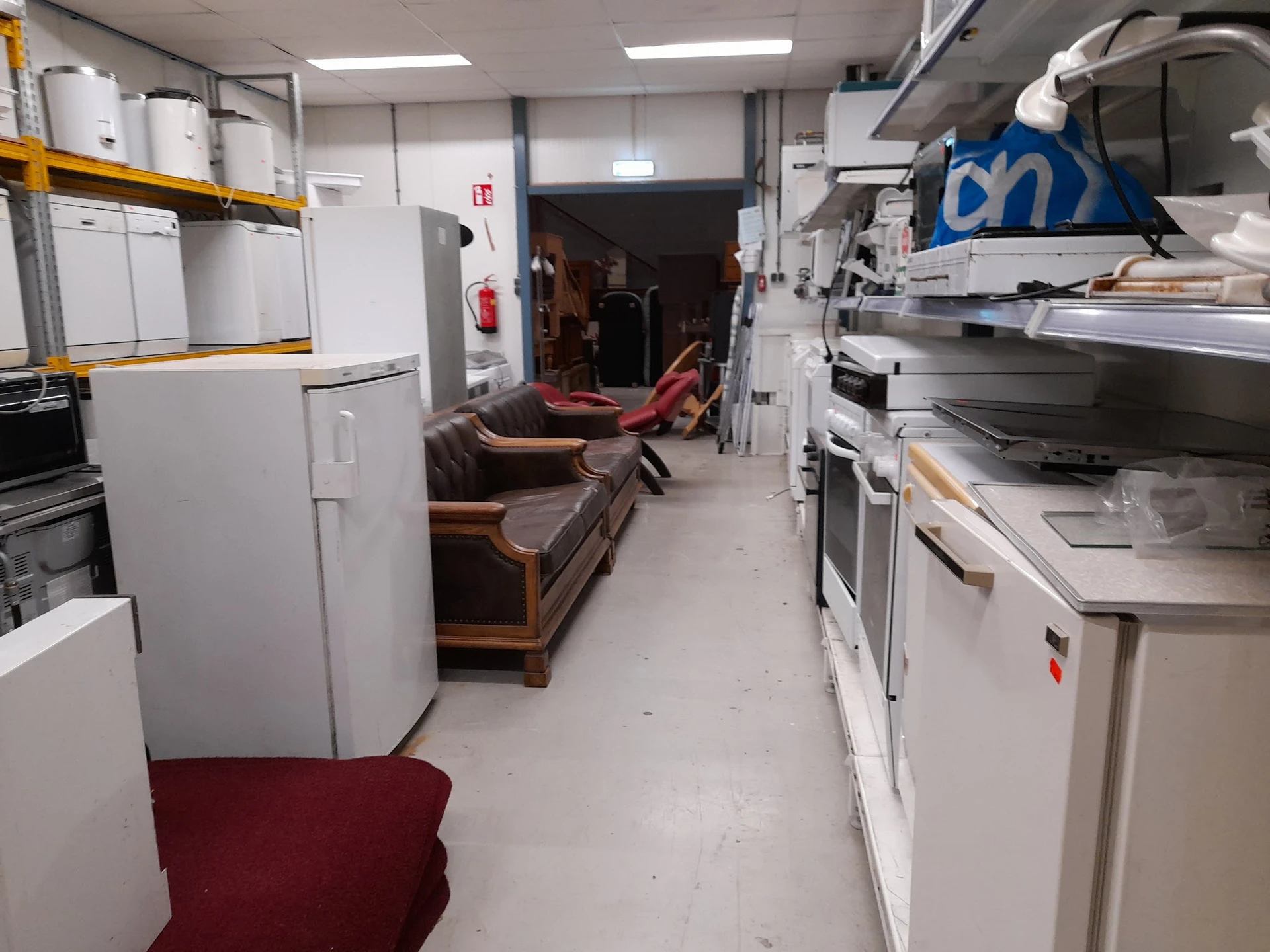 Werkruimte met witgoedapparaten, stellingen en een bruine bank langs de muur