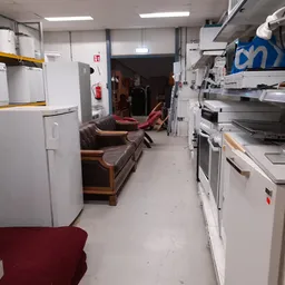 Werkruimte met witgoedapparaten, stellingen en een bruine bank langs de muur