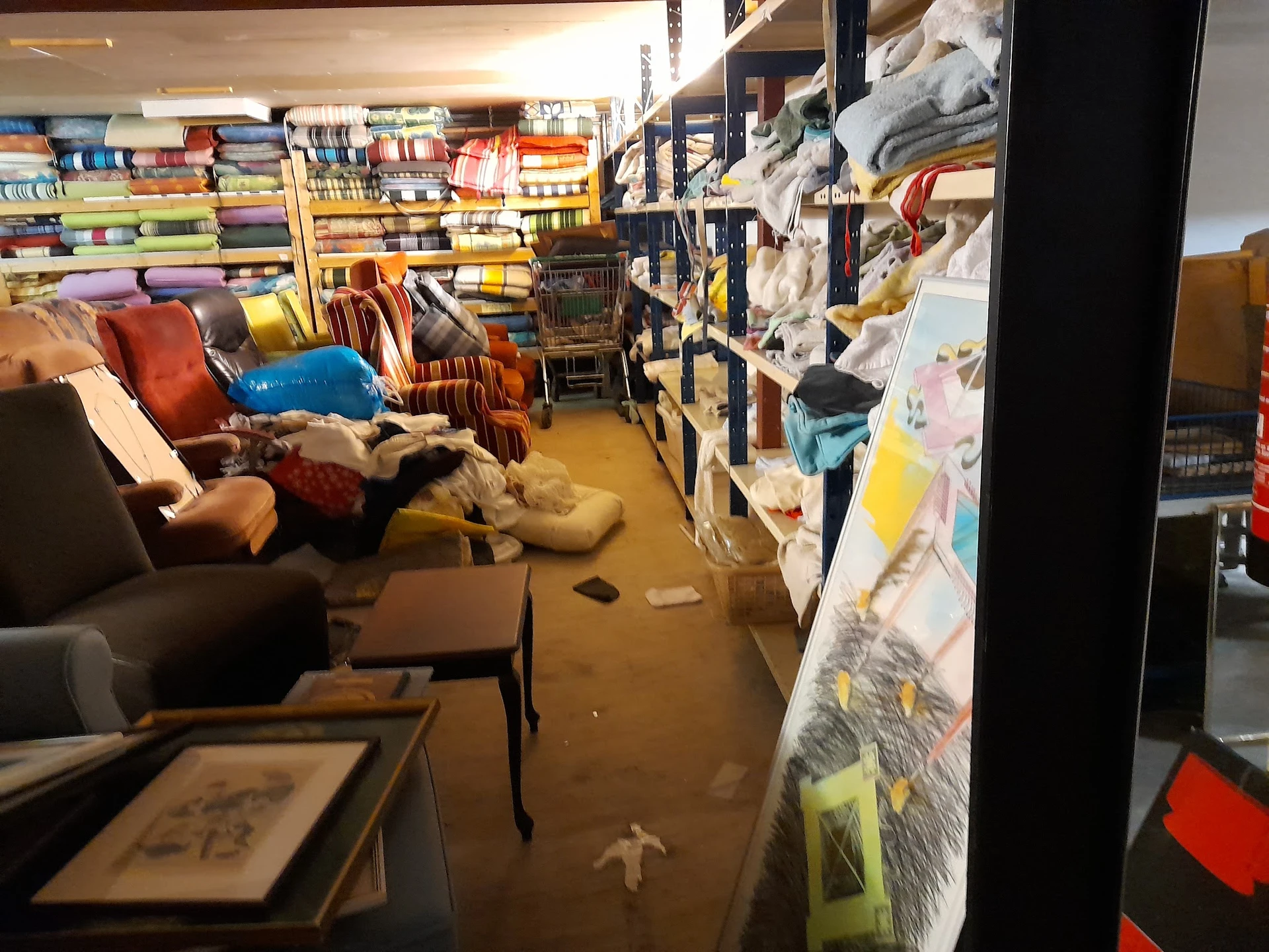 Rommelige winkelruimte met boeken op planken, meubels en spullen op de vloer
