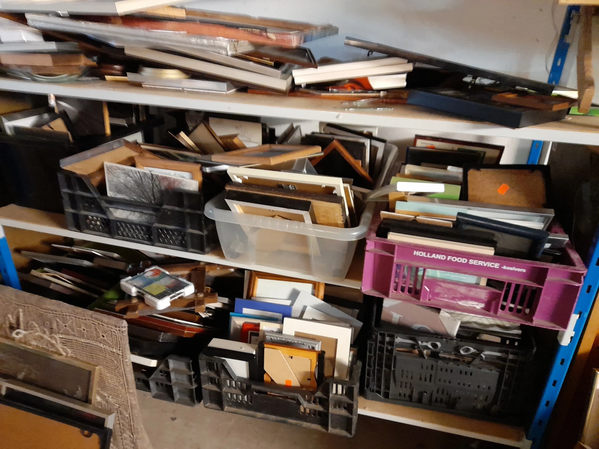 Stellingen vol met gemengde tweedehands spullen, boeken, dozen en huishoudartikelen in ongeorganiseerde opstelling