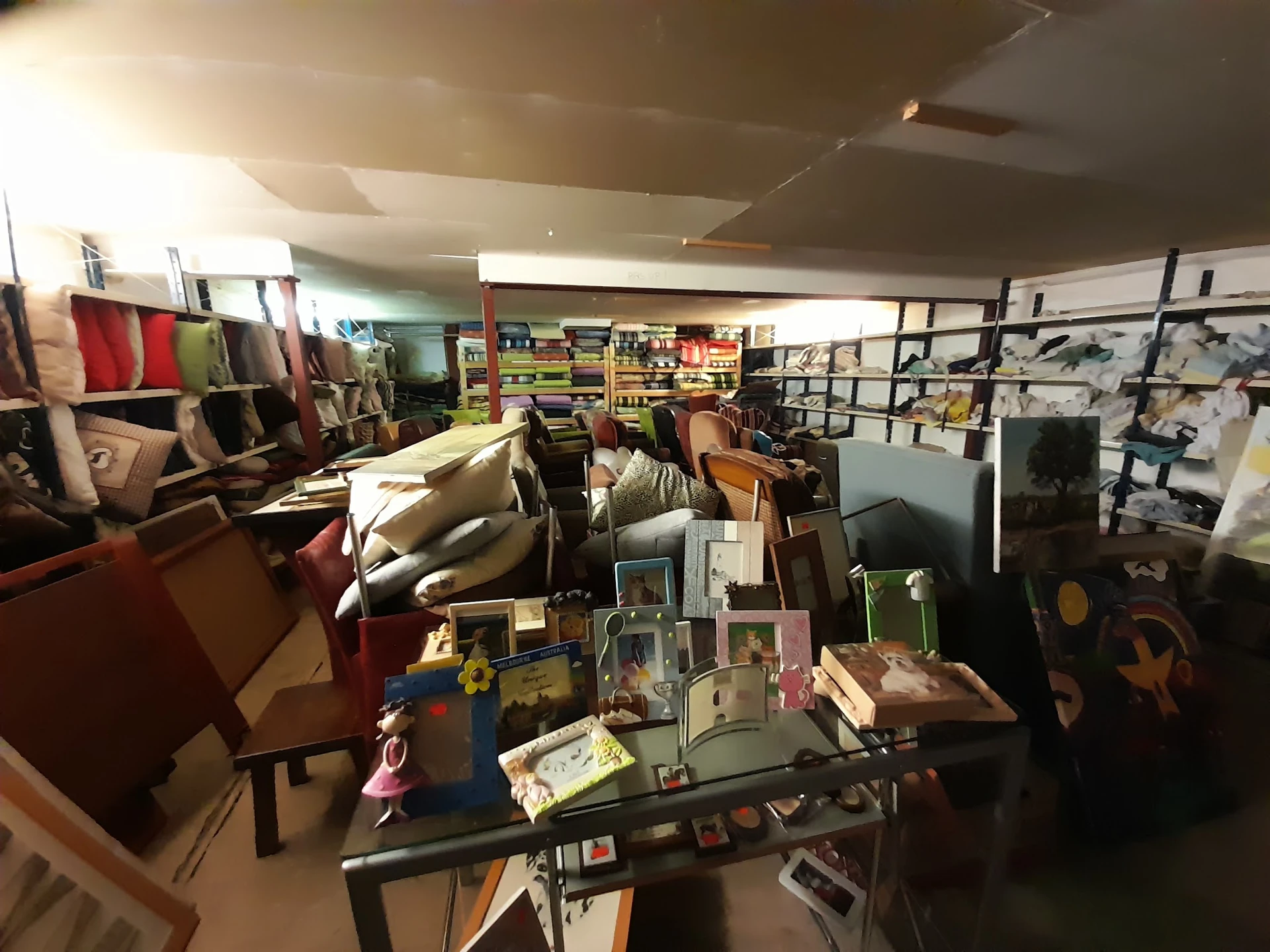 Binnenaanzicht van kringloopwinkel met tafels met spullen, meubels en stellingen langs de wanden