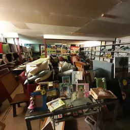 Binnenaanzicht van kringloopwinkel met tafels met spullen, meubels en stellingen langs de wanden