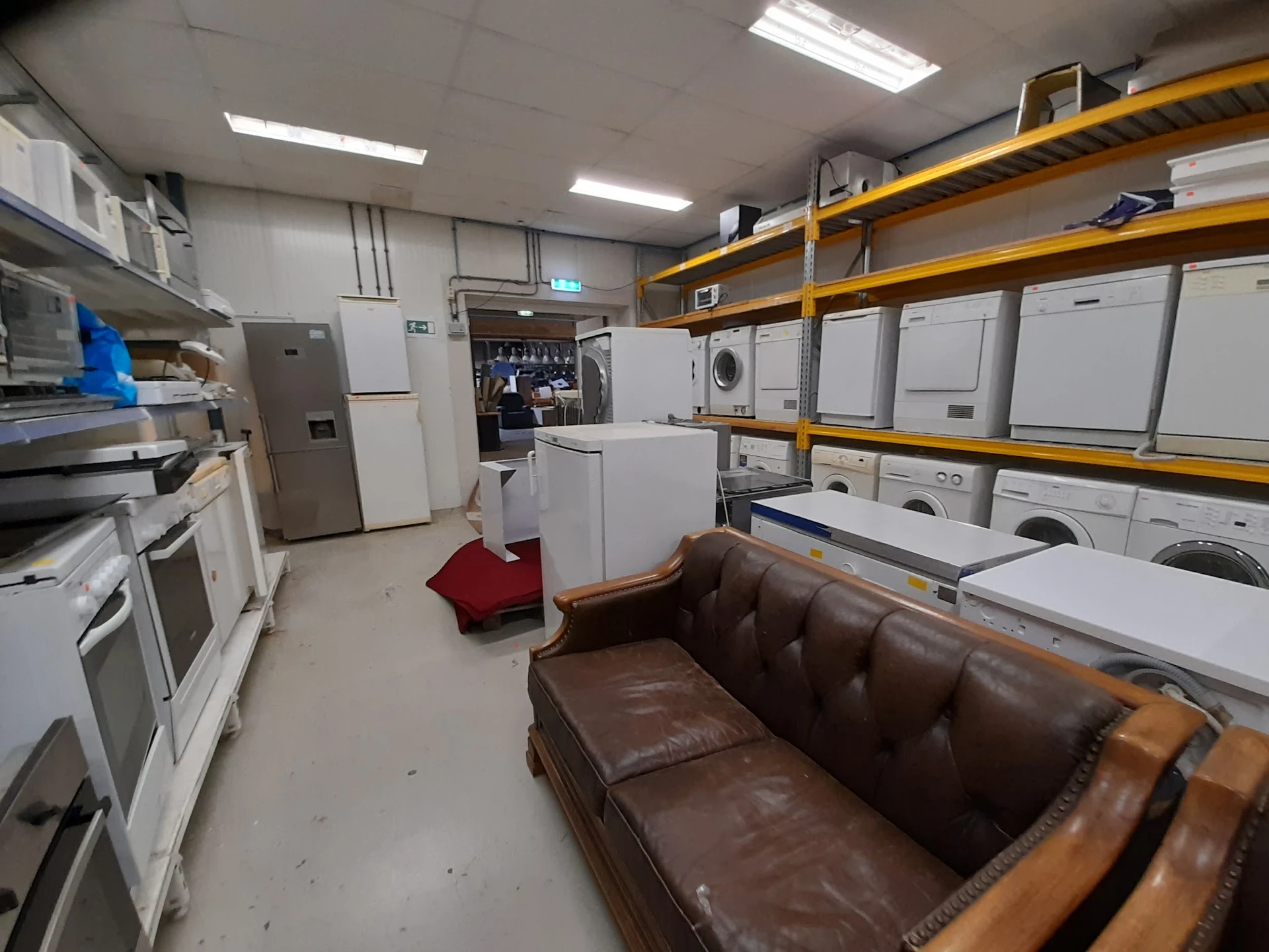 Winkelvloer met bruine leren bank, witte witgoedapparatuur op gele stellingen, ovens en koelkasten