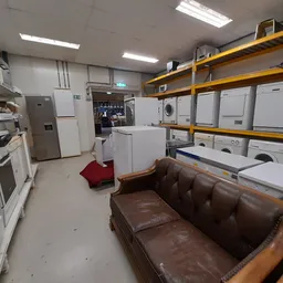 Winkelvloer met bruine leren bank, witte witgoedapparatuur op gele stellingen, ovens en koelkasten