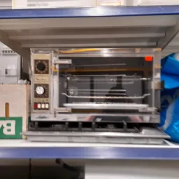 Close-up van een vintage elektrische oven/grill op een plank met blauwe stof ernaast