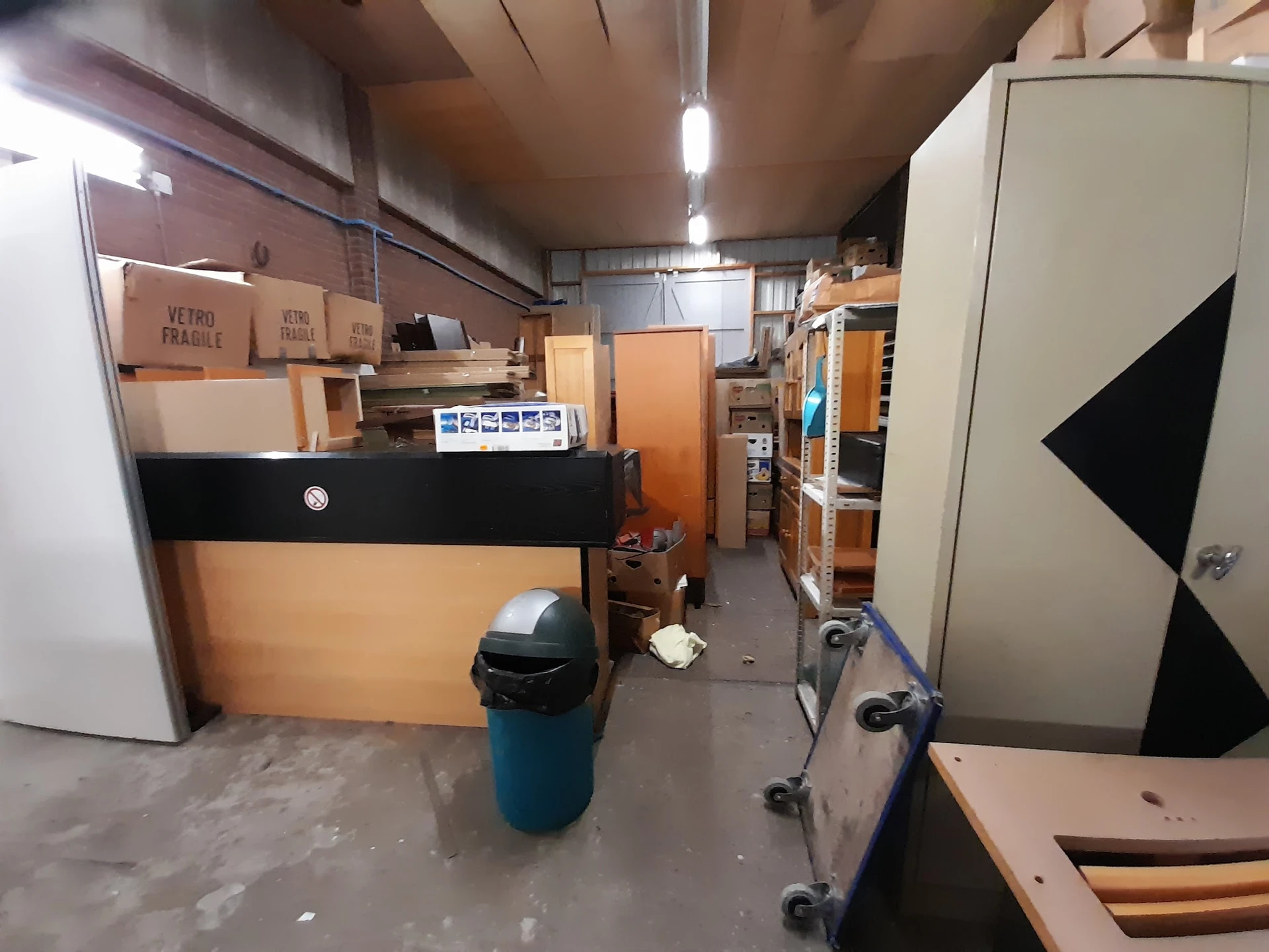 Winkelvloer met stellingen, kartonnen dozen, een vuilnisbak en diverse meubels in een kringloopwinkel