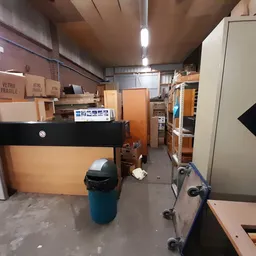 Winkelvloer met stellingen, kartonnen dozen, een vuilnisbak en diverse meubels in een kringloopwinkel