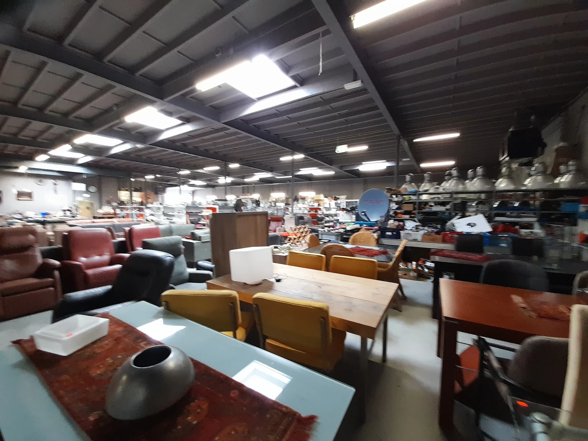 Winkelvloer met meubels zoals stoelen, tafels en kasten, verlicht door industriële plafondlampen