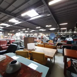 Winkelvloer met meubels zoals stoelen, tafels en kasten, verlicht door industriële plafondlampen