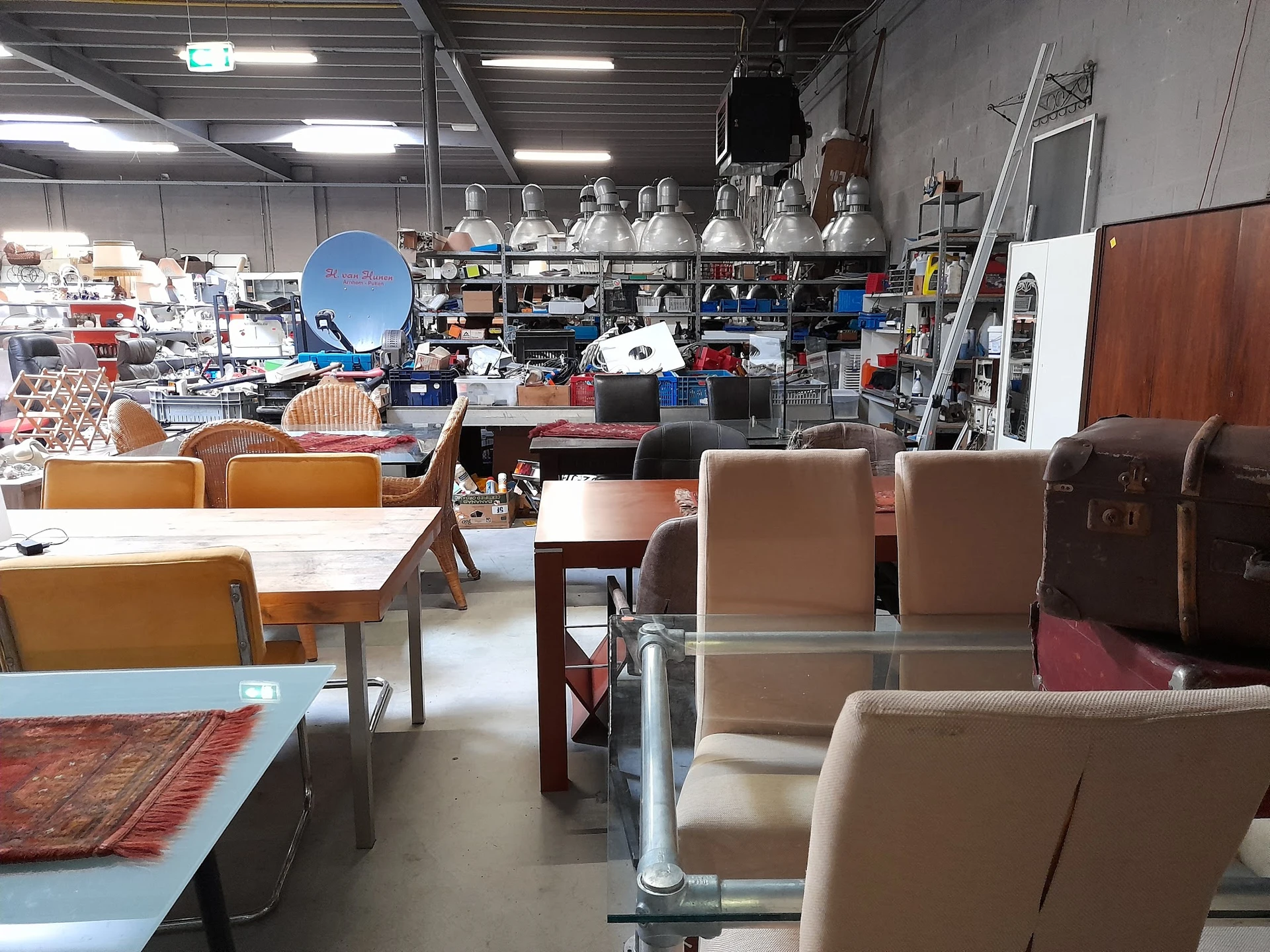 Winkelvloer met diverse meubels: stoelen, tafels en kasten tussen stellingen met huishoudartikelen op de achtergrond