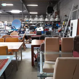 Winkelvloer met diverse meubels: stoelen, tafels en kasten tussen stellingen met huishoudartikelen op de achtergrond