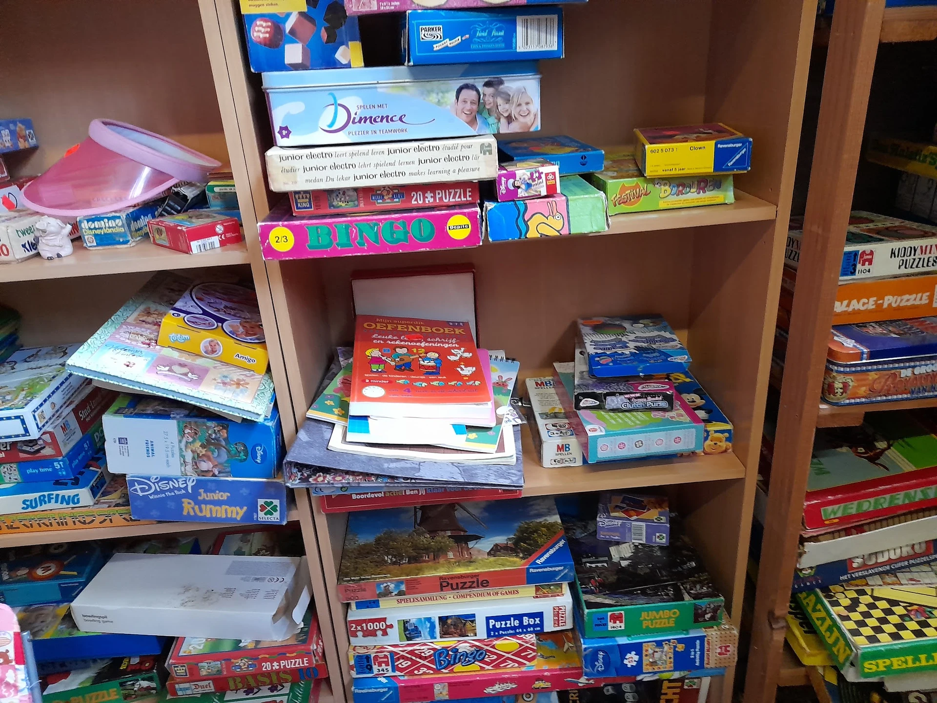 Houten stellingkast vol met dozen bordspellen, puzzels en speelgoed in een kringloopwinkel