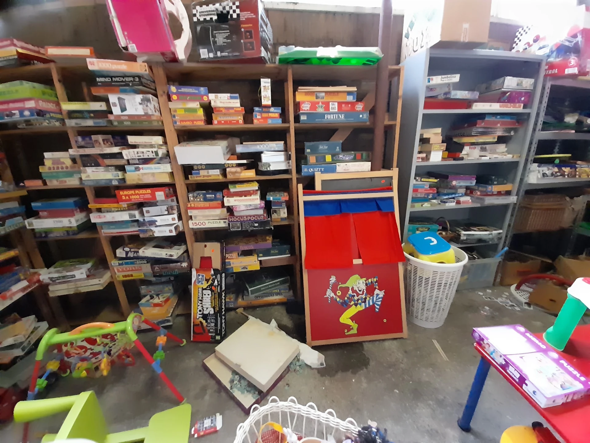 Winkelinterieur met houten stellingen vol dozen, games en speelgoed, en in het midden een rode speelgoedkast