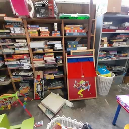 Winkelinterieur met houten stellingen vol dozen, games en speelgoed, en in het midden een rode speelgoedkast