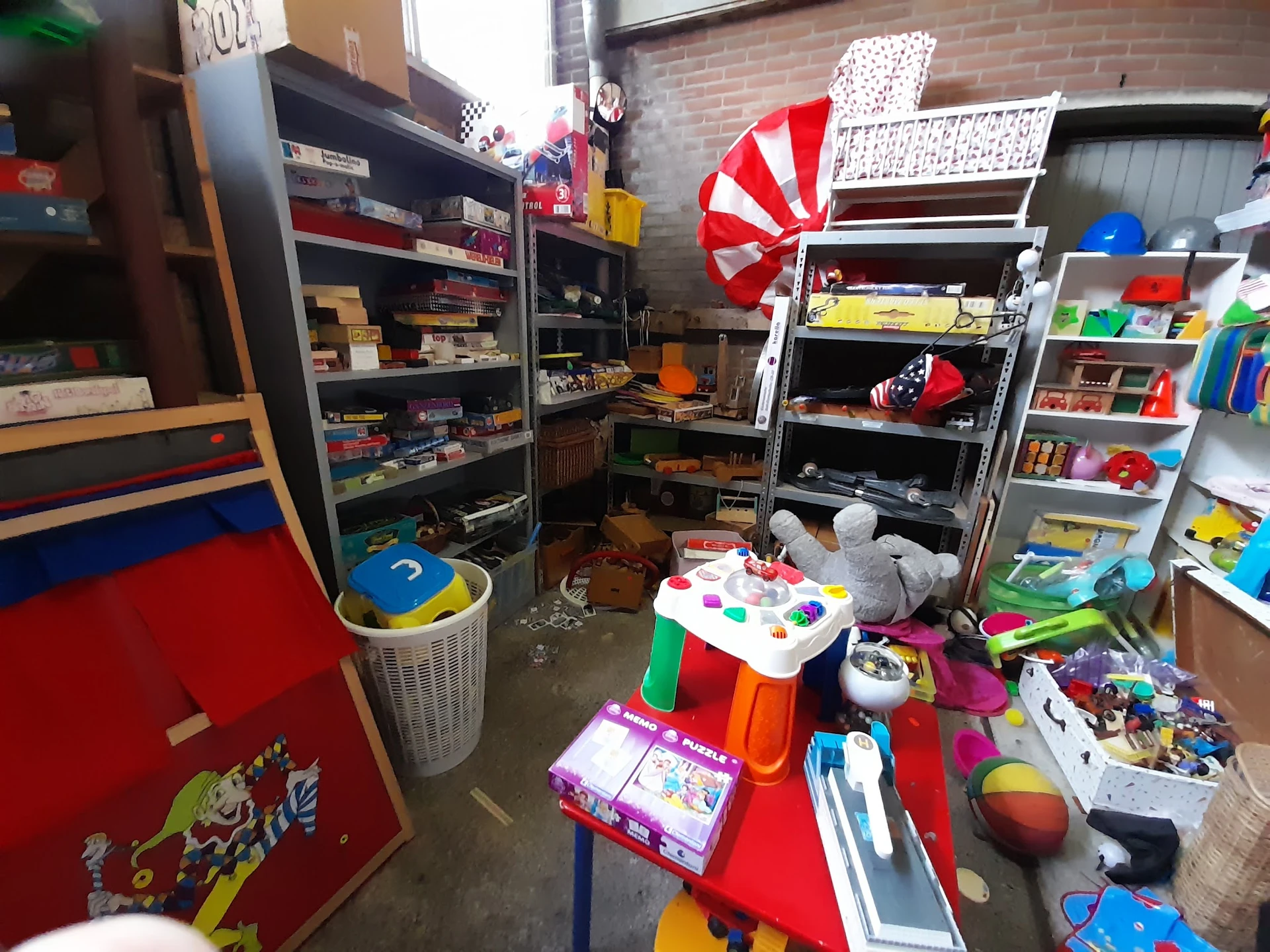 Rommelig interieur van kringloopwinkel met speelgoed, dozen en artikelen op de vloer en in stellingen