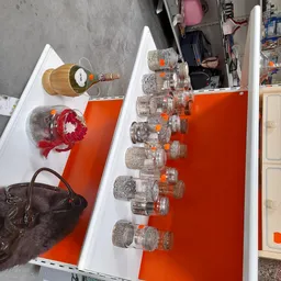 Uitgestalde items in kringloopwinkel: glazen potten met oranje dop, houten flessenhouder, rode kroon-decoratie en zwarte tas