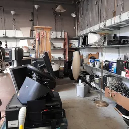 Werkplaats of opslagruimte met diverse huishoudelijke artikelen, apparaten en materialen op stellingen en vloer
