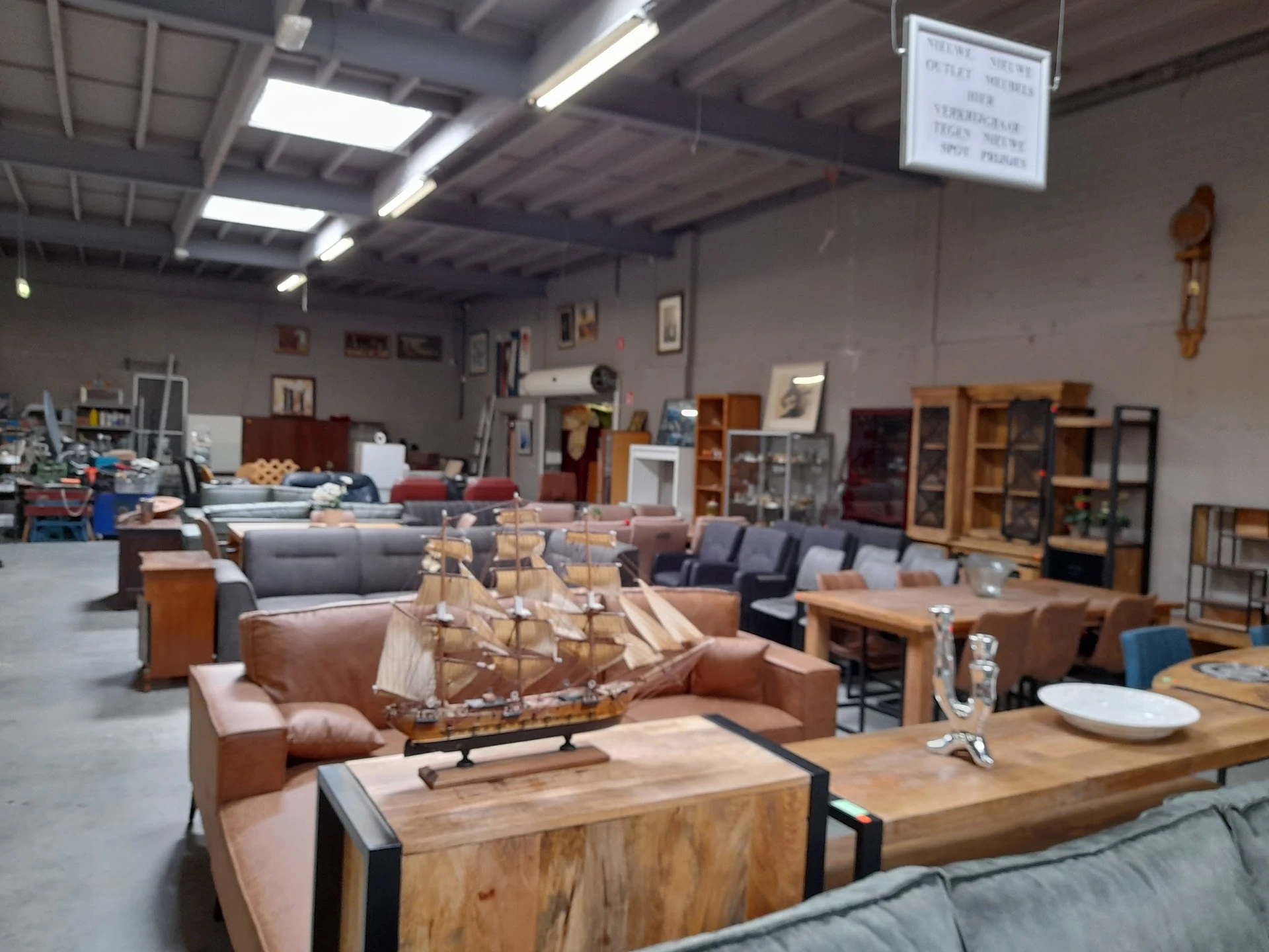 Winkelvloer met meubels: bruine fauteuils, houten tafels, kasten en een scheepsmodel op tafel, overzicht van het aanbod