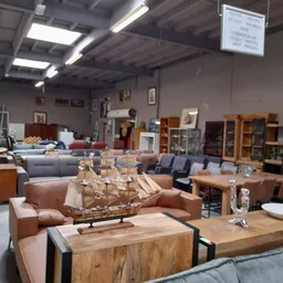 Winkelvloer met meubels: bruine fauteuils, houten tafels, kasten en een scheepsmodel op tafel, overzicht van het aanbod