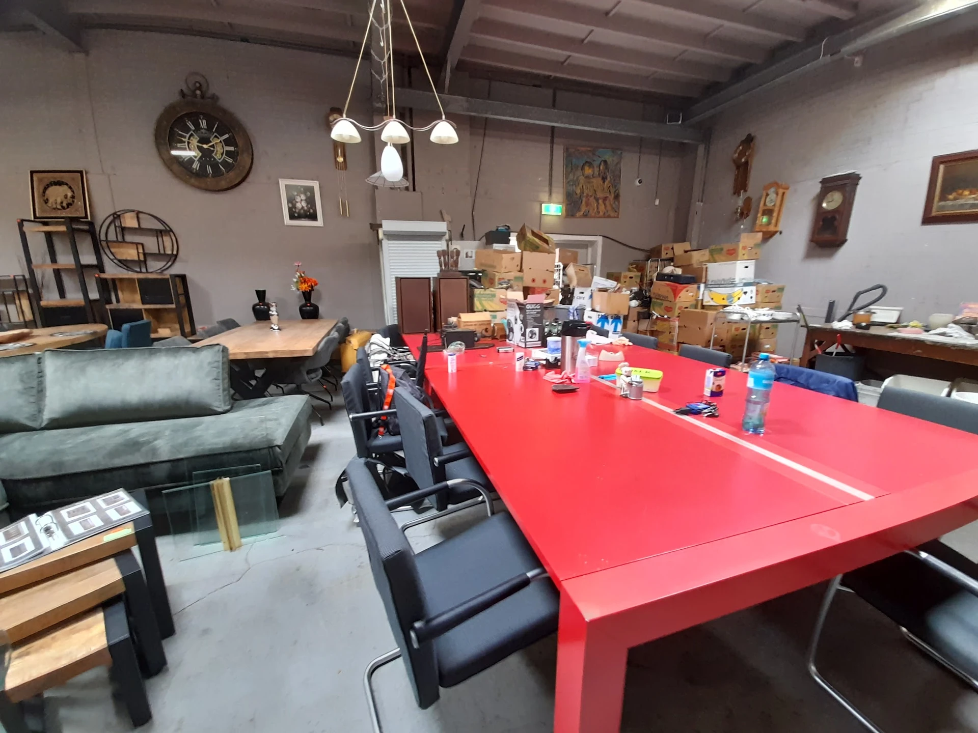 Grote ruimte met rode tafel, zwarte stoelen, groene bank en diverse meubels en dozen op de achtergrond