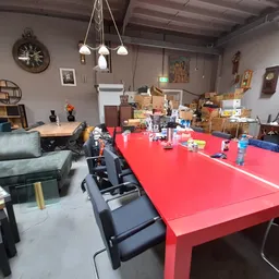 Grote ruimte met rode tafel, zwarte stoelen, groene bank en diverse meubels en dozen op de achtergrond