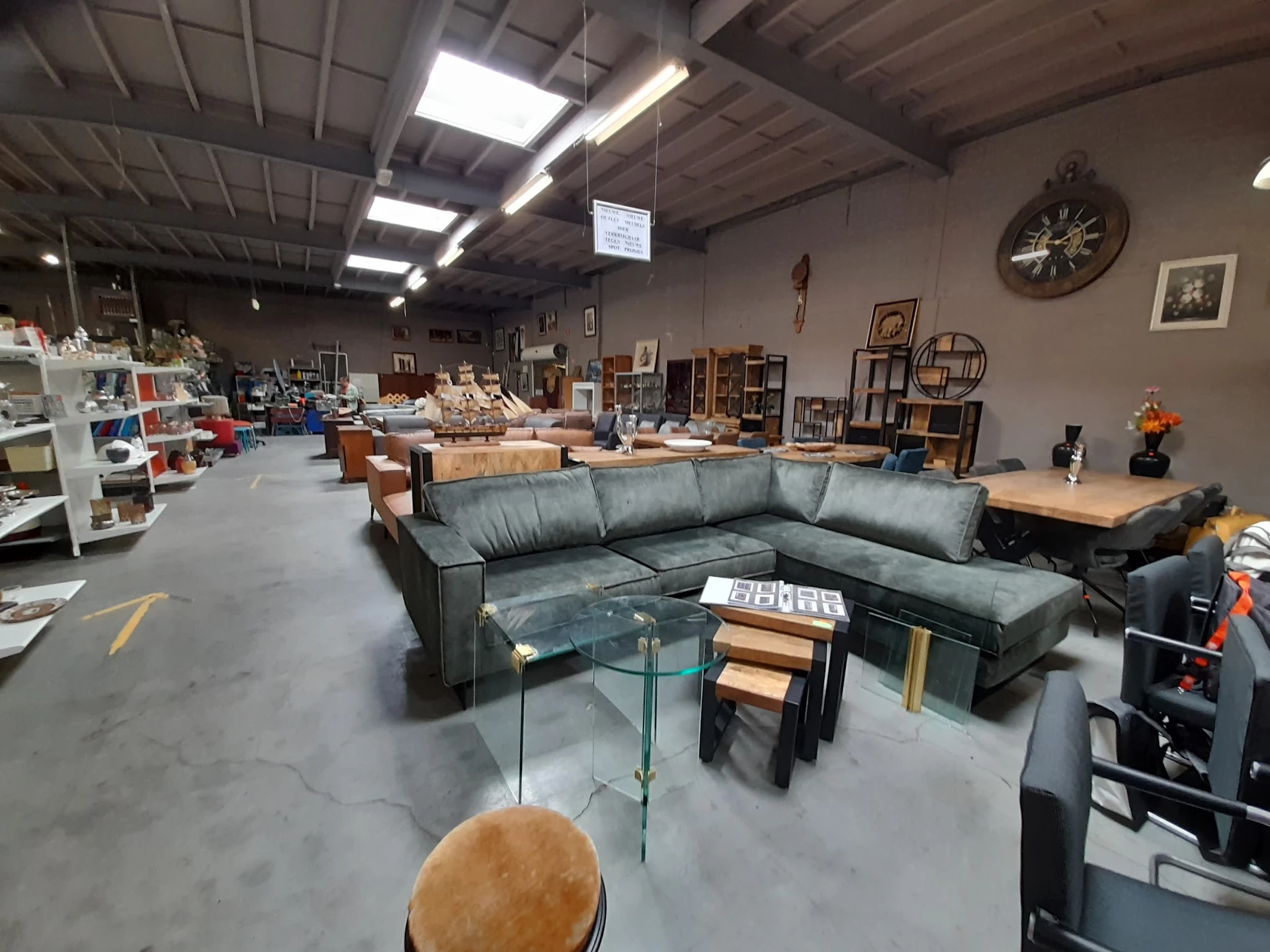 Winkelvloer met grijze hoekbank, glazen salontafel en diverse meubels en decoratiestukken in het magazijn
