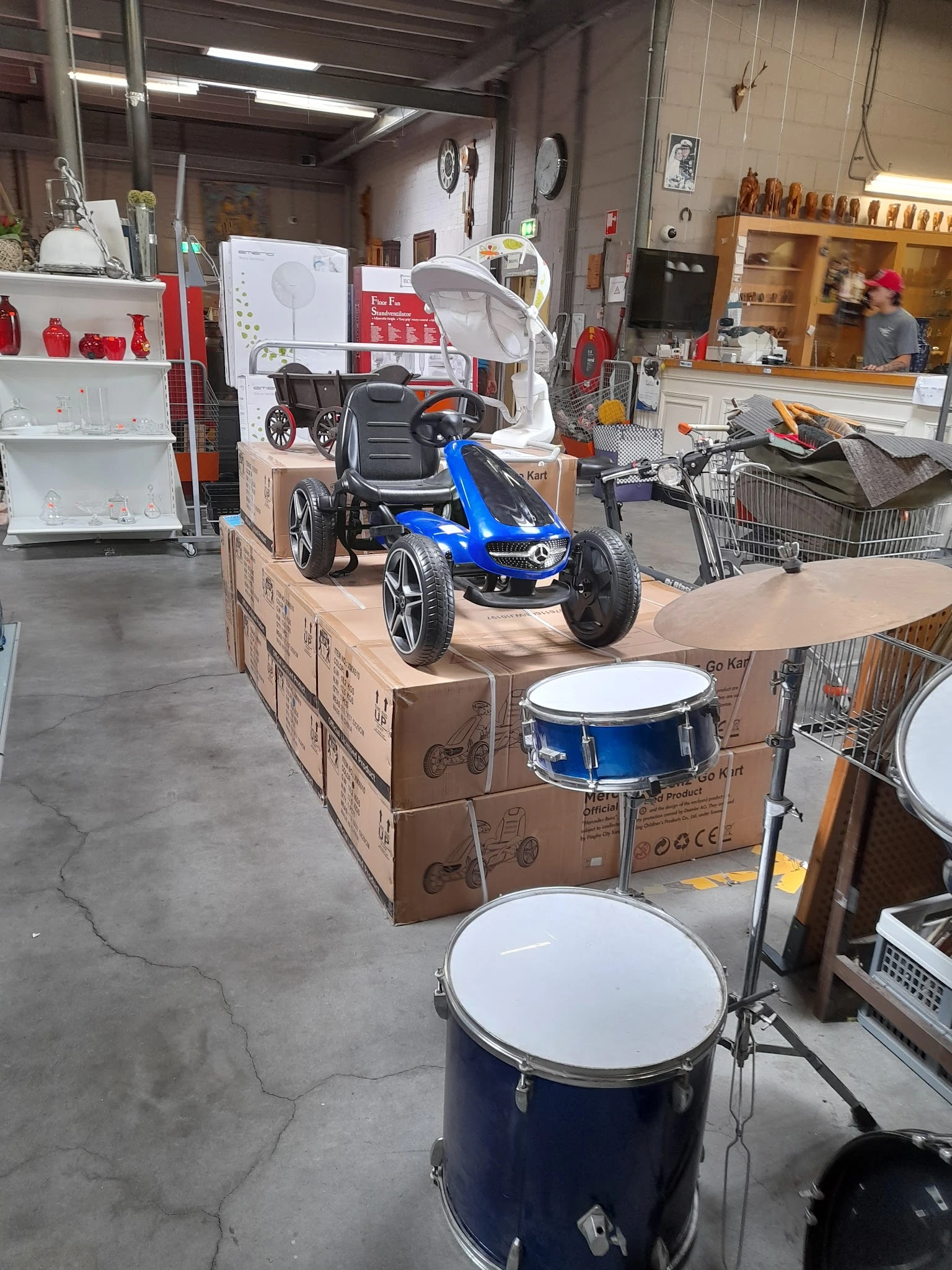 Blauwe kindergo-kart en trommel op kartonnen dozen in kringloopwinkel