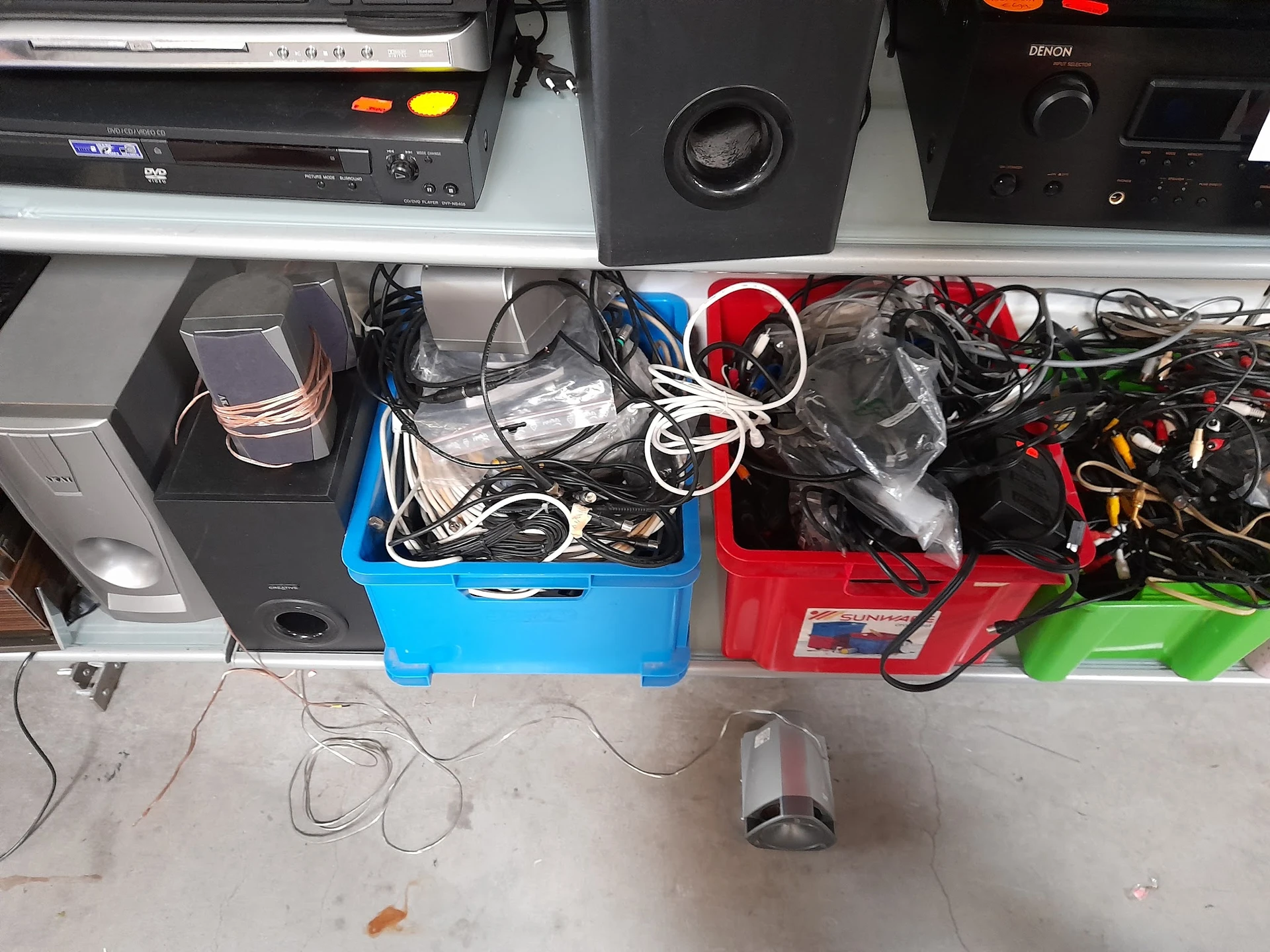 Blauwe en rode kunststofkisten met elektronische apparaten, kabels en accessoires op een werkblad