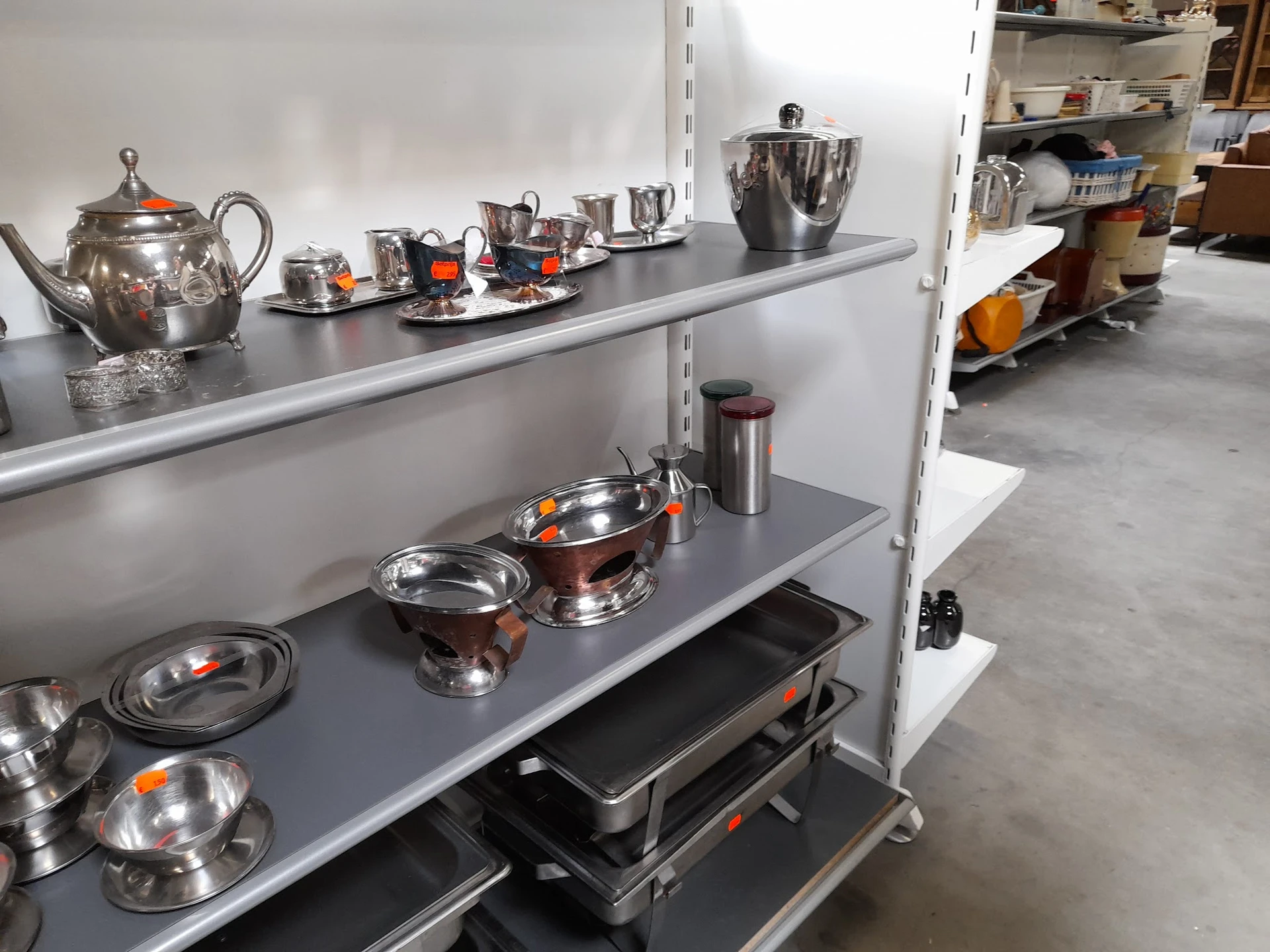 Stellage met zilverkleurig serviesgoed, theepotten en schalen met oranje accenten
