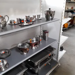 Stellage met zilverkleurig serviesgoed, theepotten en schalen met oranje accenten