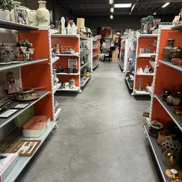 Winkelvloer van kringloopwinkel met witte stellingen met oranje achterwanden, volgestouwd met diverse huishoudelijke artikele