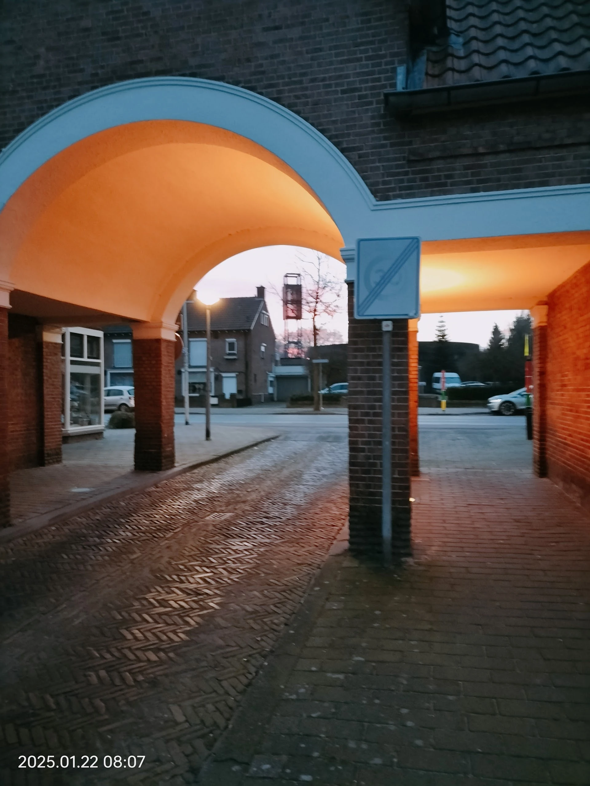 Ingang van kringloopwinkel met oranje afdak en bakstenen kolommen, uitzicht op straat met huizen
