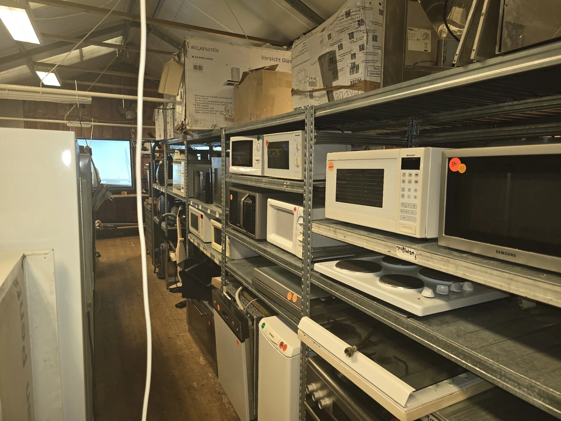Diverse gebruikte magnetrons en ovens op metalen stellingkasten in een kringloopwinkel