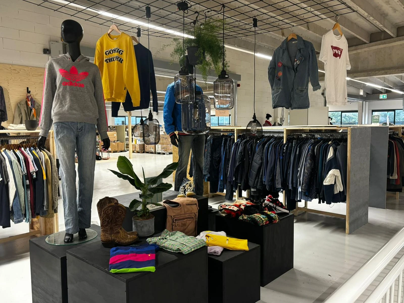 Winkelinterieur met kledingrekken, etalagepoppen en een zwarte display-tafel met kleding en groene plant