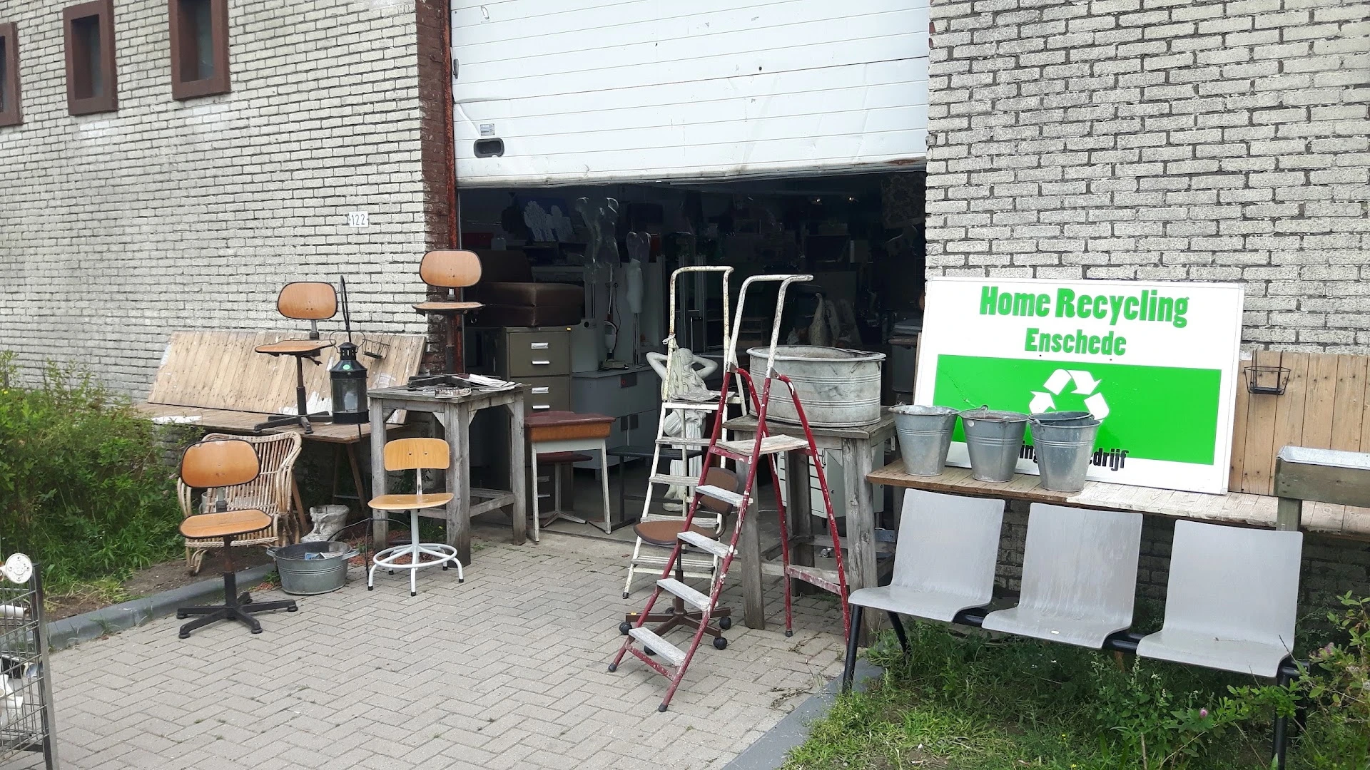 Gebruikte meubels en huishoudartikelen buiten uitgestald, waaronder stoelen, trapladders en containers