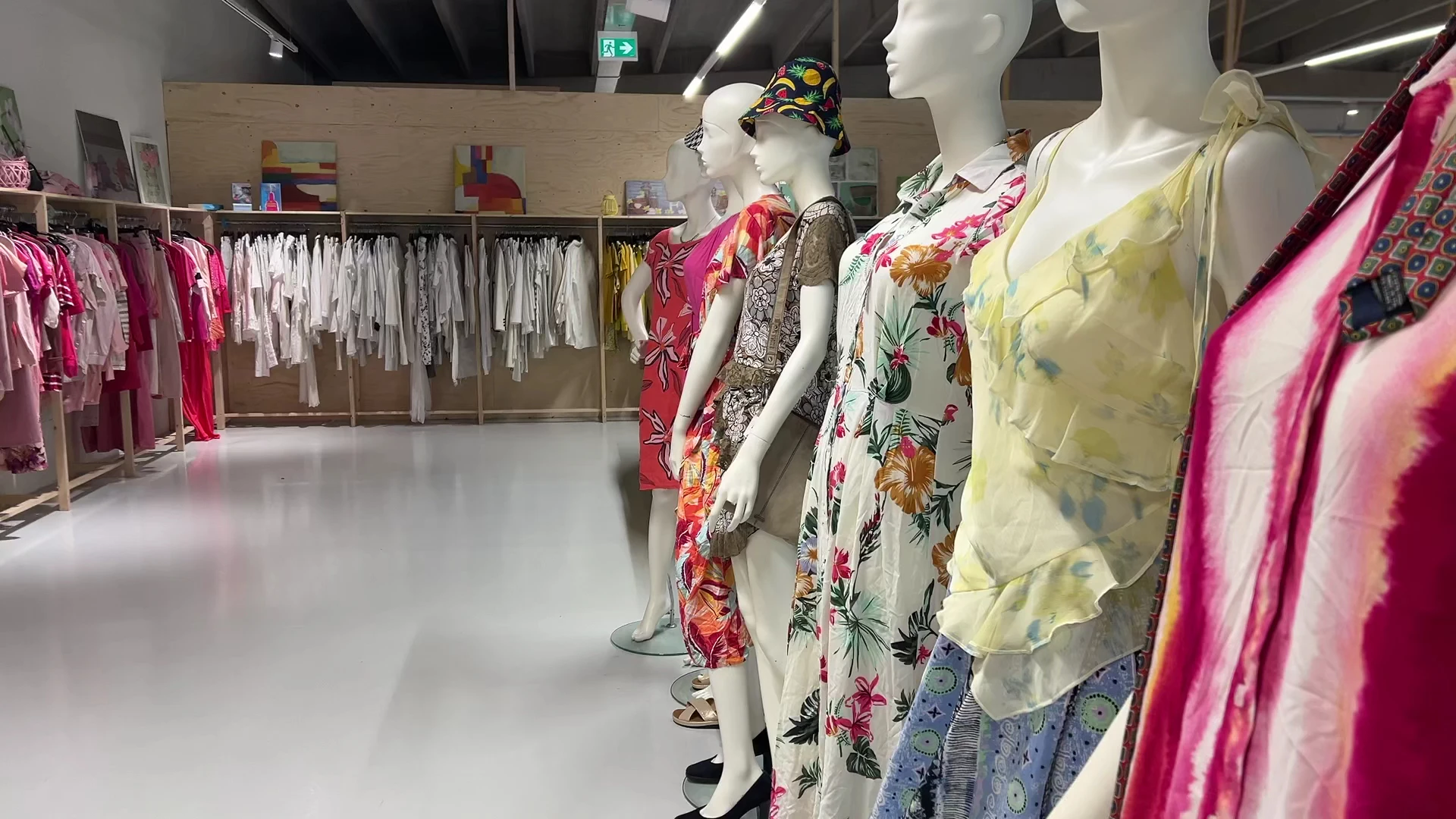 Etalage met mannequins in kleurrijke zomer- en bloemenjurken, op de achtergrond rekken met kleding