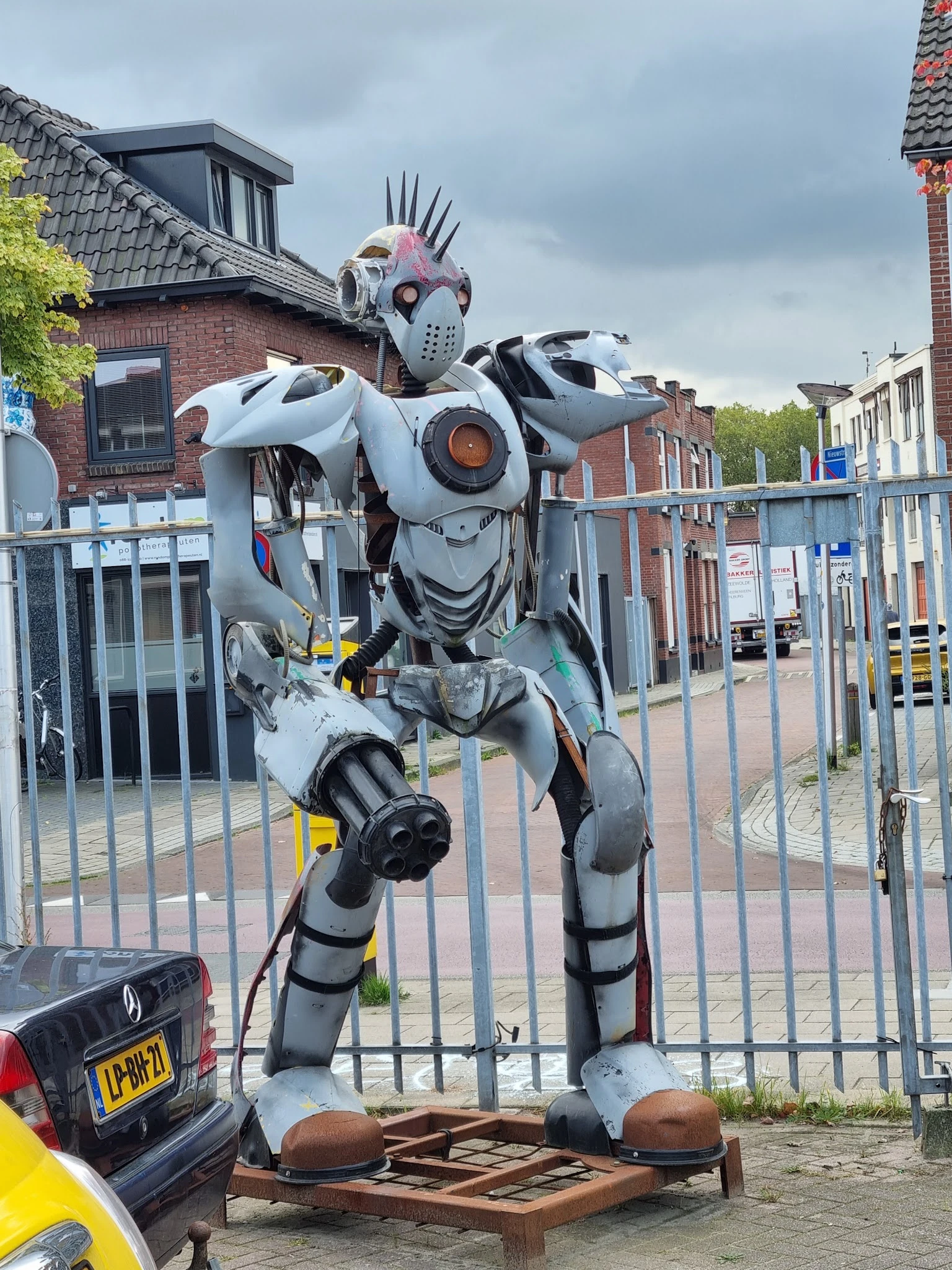 Grote witte en grijze robot-sculptuur achter metalen hek buiten de winkel