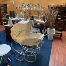 Vintage kinderwagen met crèmekleurig canvas en zilveren frame op blauwe vloer in kringloopwinkel